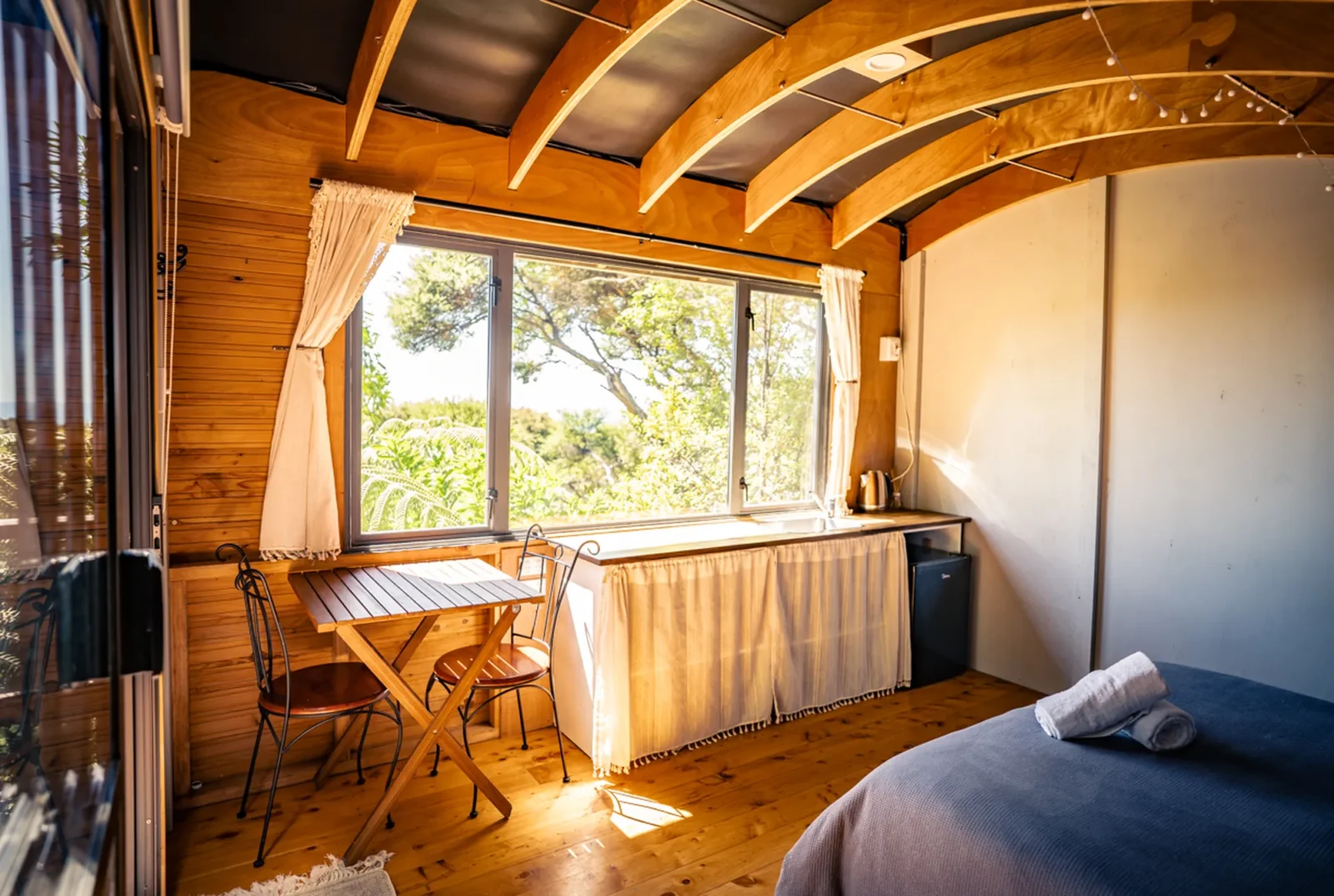Bedroom with arched wooden ceiling and large windows in The Outpost cabin at Totara Enclave