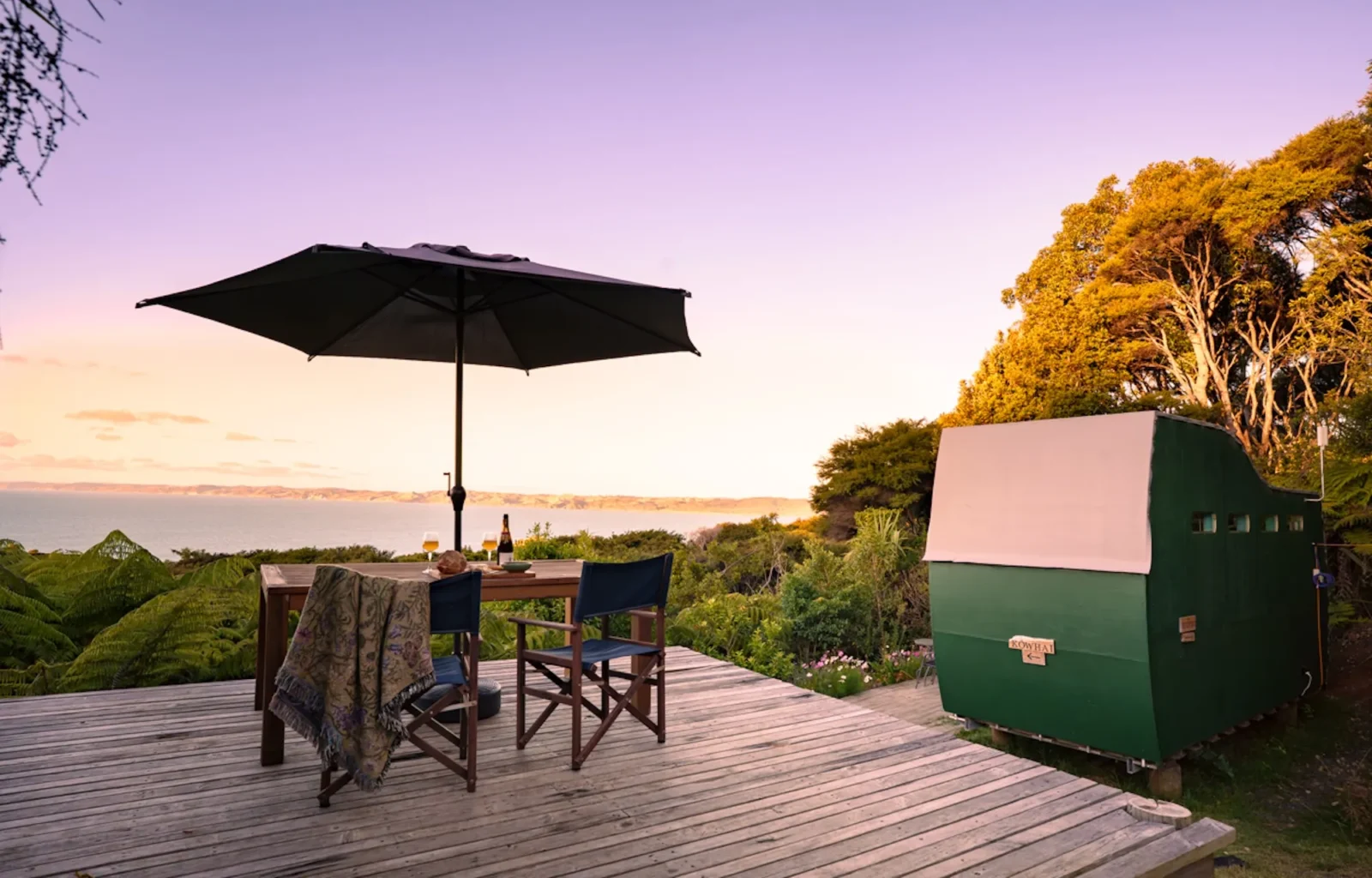 Outdoor deck with umbrella and chairs overlooking the sunset at Totara Enclave